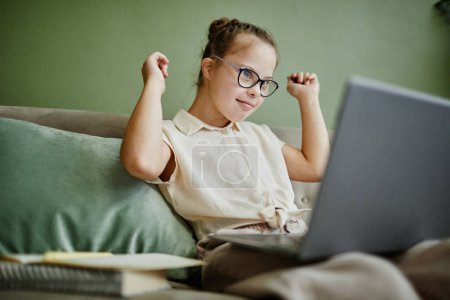 Photo for Portrait of happy girl with down syndrome cheering while watching online lesson at home via laptop - Royalty Free Image