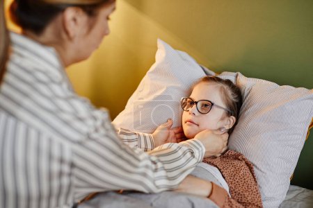 Photo for Portrait of caring mother tucking in child with down syndrome at bedtime, copy space - Royalty Free Image