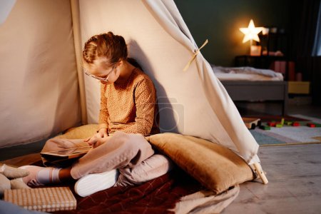 Téléchargez les photos : Portrait of young girl with down syndrome using tablet in cozy play tent at night, copy space - en image libre de droit