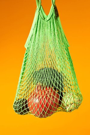 Photo for Vertical close up of fresh vegetables in eco net bag against vibrant orange background, conscious consumption - Royalty Free Image