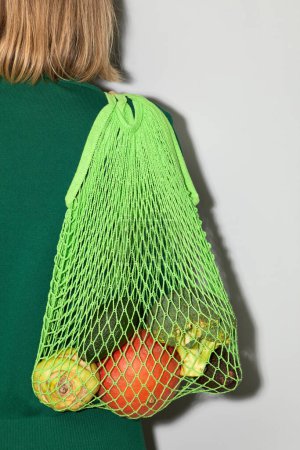 Photo for Close up of unrecognizable woman carrying green eco bag with vegetables against minimal background, conscious consumption and organic food concept - Royalty Free Image