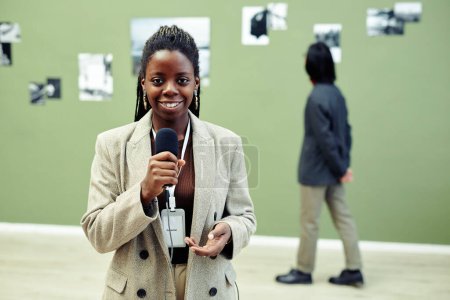 Téléchargez les photos : Portrait horizontal moyen du jeune conservateur de la galerie d'art afro-américaine tenant un microphone parlant de l'exposition actuelle - en image libre de droit
