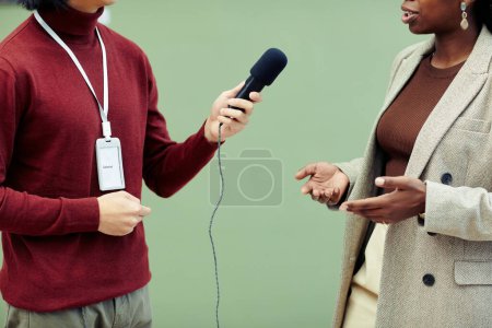 Téléchargez les photos : Section moyenne de jeune galeriste tenant microphone prenant interview de photographe afro-américaine le jour de l'exposition dans la galerie d'art - en image libre de droit