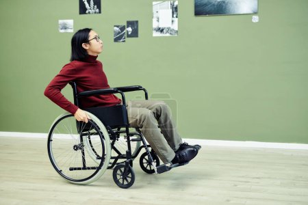 Téléchargez les photos : Portrait de jeune homme asiatique moderne avec handicap en fauteuil roulant visitant exposition de photographie abstraite dans la galerie d'art - en image libre de droit