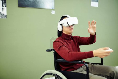 Téléchargez les photos : Jeune homme asiatique handicapé portant casque VR et écouteurs visitant exposition de photographie contemporaine dans la galerie d'art - en image libre de droit