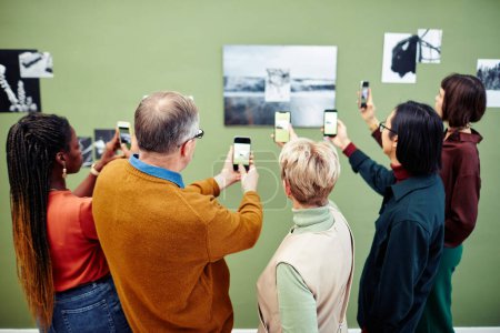 Photo for Group of multi-ethnic visitors scanning QR code to get more information about black and white photo on wall at exhibition in museum - Royalty Free Image
