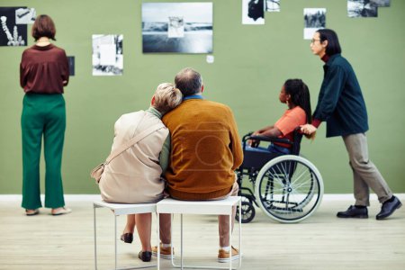 Téléchargez les photos : Groupe de personnes âgées et les jeunes passent du temps libre dans la galerie d'art moderne en regardant des photos abstraites et de détente - en image libre de droit
