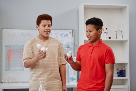 Photo for Waist up portrait of two teenage boys holding molecule models while giving presentation in chemistry class - Royalty Free Image
