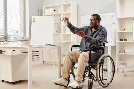 Photo for Full length portrait of African American teacher in wheelchair holding glass beaker during chemistry class in school, copy space - Royalty Free Image