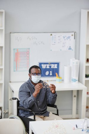 Photo for Vertical portrait of African American teacher wearing mask and holding molecule model during chemistry class in school - Royalty Free Image