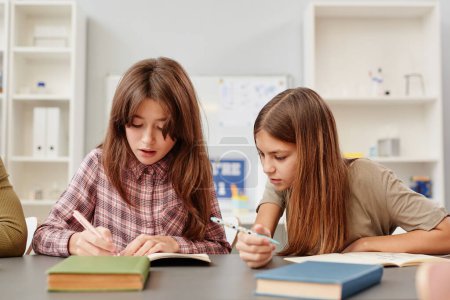 Photo for Portrait of young girl looking into friends notebook while copying test answers in school - Royalty Free Image