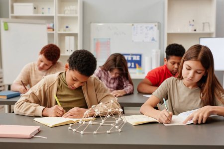 Foto de Retrato de vista frontal de un grupo diverso de niños que estudian en escritorios en el aula de la escuela con modelo de química en primer plano - Imagen libre de derechos