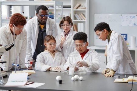 Téléchargez les photos : Groupe diversifié d'enfants portant des blouses de laboratoire en classe de chimie tout en appréciant les expériences scientifiques - en image libre de droit