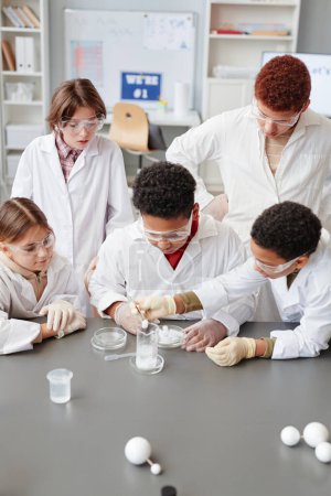 Photo for High angle view at diverse group of children enjoying science experiments in chemistry class and wearing lab coats - Royalty Free Image