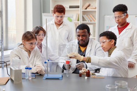 Téléchargez les photos : Portrait d'un enseignant afro-américain démontrant des expériences scientifiques à divers groupes d'enfants dans un laboratoire de chimie à l'école - en image libre de droit