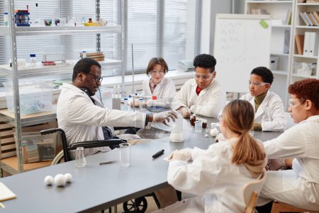 Téléchargez les photos : Vue en grand angle chez un professeur afro-américain démontrant des expériences scientifiques à divers groupes d'enfants dans un laboratoire de chimie à l'école - en image libre de droit