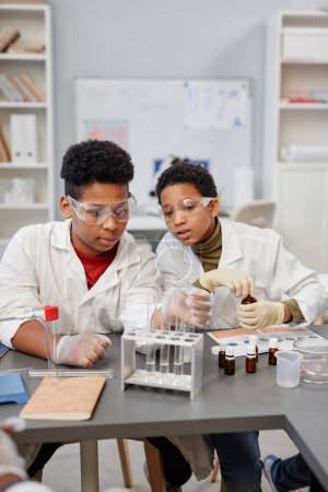 Foto de Retrato vertical de dos curiosos niños afroamericanos viendo experimentos científicos en el laboratorio de química de la escuela - Imagen libre de derechos