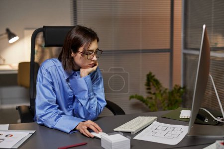 Téléchargez les photos : Portrait latéral d'une jeune femme d'affaires fatiguée qui utilise un ordinateur sur son lieu de travail et qui travaille tard dans la nuit au bureau - en image libre de droit