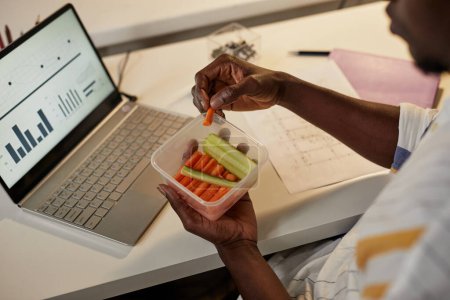 Photo for High angle closeup of young African American man eating healthy snack while working or studying late at night, copy space - Royalty Free Image