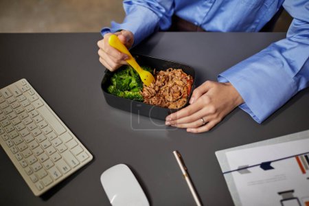 Téléchargez les photos : Gros plan de jeune femme d'affaires mangeant des plats à emporter au bureau tout en travaillant tard dans la nuit au bureau, espace de copie - en image libre de droit
