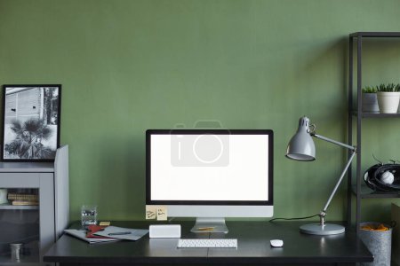 Téléchargez les photos : Image de fond du bureau à domicile avec écran d'ordinateur vierge contre le mur vert, espace de copie - en image libre de droit