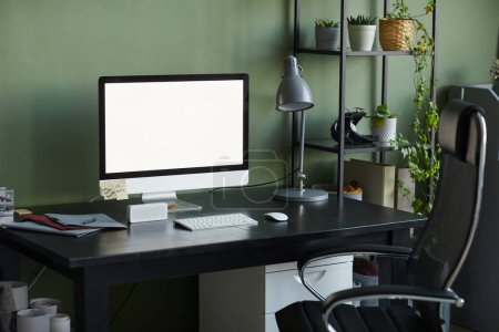 Téléchargez les photos : Image de fond du bureau à domicile avec écran d'ordinateur vierge sur le bureau contre le mur vert, espace de copie - en image libre de droit
