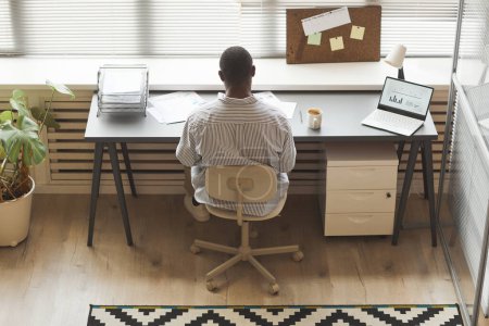 Foto de Vista superior mínima del empresario negro analizando documentos mientras trabaja por ventana en la oficina, espacio de copia - Imagen libre de derechos