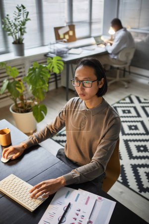 Téléchargez les photos : Portrait vertical de développeur de logiciels asiatiques utilisant l'ordinateur tout en travaillant tard au bureau - en image libre de droit
