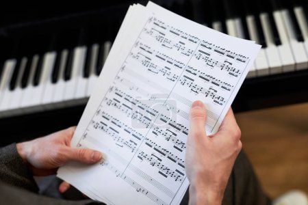 Téléchargez les photos : Gros plan du musicien tenant la partition et les examinant avant de jouer du piano - en image libre de droit