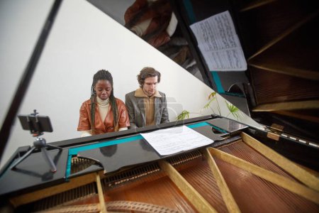 Téléchargez les photos : Jeune couple assis ensemble et jouant du piano à queue pendant la leçon de musique à la classe - en image libre de droit