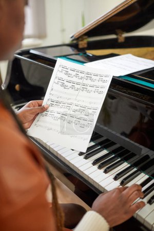 Photo for Close-up of African woman examining the paper with notes while sitting at grand piano and learning to play music at lesson - Royalty Free Image