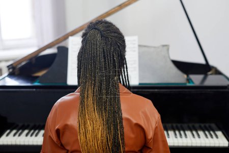 Foto de Vista trasera de una mujer joven con un peinado elegante tocando el piano de cola durante la lección en la escuela musical - Imagen libre de derechos