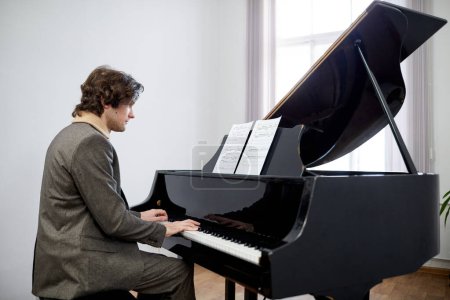 Téléchargez les photos : Jeune pianiste jouant du piano à queue, il regarde des partitions et joue de la musique classique à l'école - en image libre de droit