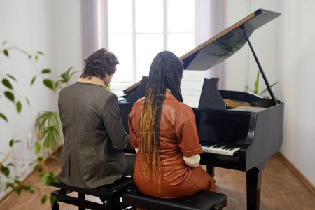 Foto de Vista trasera de la joven pareja tocando la composición clásica en piano de cola juntos en el aula - Imagen libre de derechos