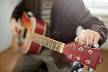 Photo for Close-up of young man sitting and tuning the strings of guitar before playing the music - Royalty Free Image