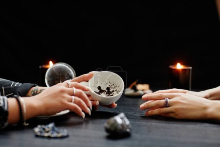 Photo for Side view close up of female fortune teller reading coffee grounds telling destiny in seance with young woman in dark - Royalty Free Image
