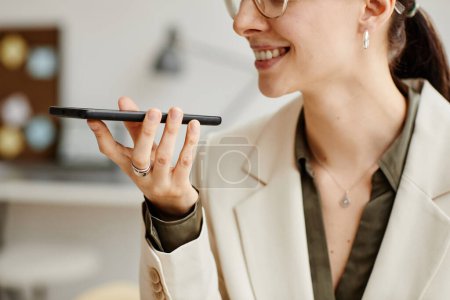 Téléchargez les photos : Vue latérale minimale d'une femme d'affaires souriante tenant un smartphone et enregistrant un message vocal - en image libre de droit