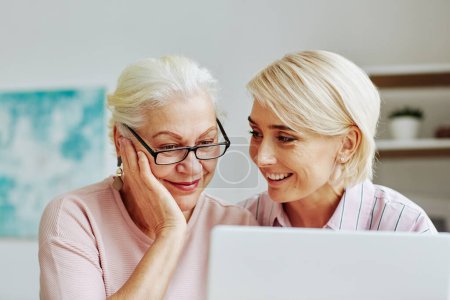 Photo for Close up portrait of smiling young woman with senior mother using laptop together at home and shopping online - Royalty Free Image