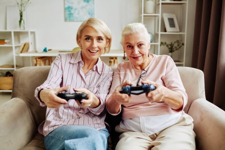 Téléchargez les photos : Portrait avant de femme âgée aux cheveux blancs jouant à des jeux vidéo avec une fille adulte dans une scène confortable à la maison - en image libre de droit