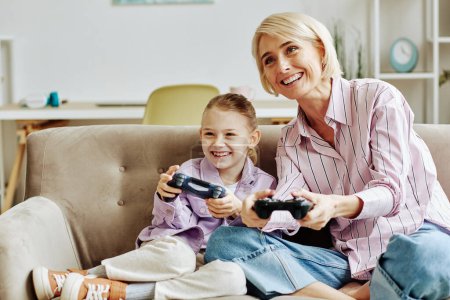 Téléchargez les photos : Portrait de jeune femme blonde jouant à des jeux vidéo avec une petite fille et s'amusant ensemble à la maison - en image libre de droit