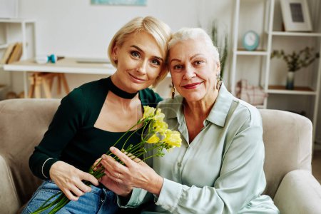 Photo for Front view portrait of adult daughter with mother looking at camera and holding flowers in cozy home scene - Royalty Free Image