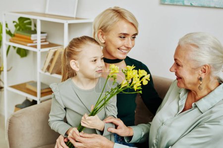 Téléchargez les photos : Portrait de petite fille donnant des fleurs à grand-mère le jour de la fête des mères, trois générations de femmes dans la famille - en image libre de droit