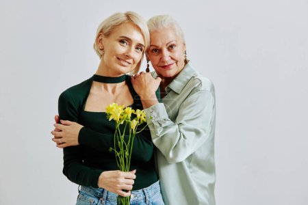 Téléchargez les photos : Portrait taille haute minime de femme âgée avec fille adulte tenant des fleurs et regardant la caméra, espace de copie - en image libre de droit