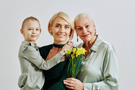 Téléchargez les photos : Portrait minimal de trois femmes en famille tenant des fleurs et souriant à la caméra en studio - en image libre de droit