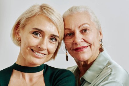 Téléchargez les photos : Portrait en gros plan d'une femme âgée souriante avec sa fille adulte regardant une caméra en studio - en image libre de droit