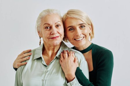 Photo for Minimal waist up portrait of smiling adult daughter with senior woman embracing and looking at camera in studio - Royalty Free Image