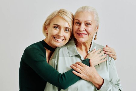 Photo for Candid waist up portrait of senior woman with adult daughter embracing in studio and looking at camera - Royalty Free Image