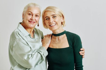 Photo for Waist up portrait of senior woman with adult daughter embracing in studio and looking at camera smiling - Royalty Free Image