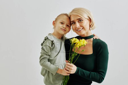 Téléchargez les photos : Portrait à la taille minime de la jeune mère avec une petite fille tenant des fleurs en studio et regardant la caméra, l'espace de copie - en image libre de droit