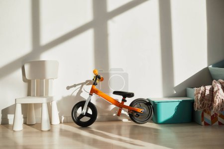 Téléchargez les photos : Image de fond minimale de vélo d'équilibre vibrant pour les tout-petits contre le mur blanc dans la chambre des enfants éclairée par la lumière du soleil, espace de copie - en image libre de droit